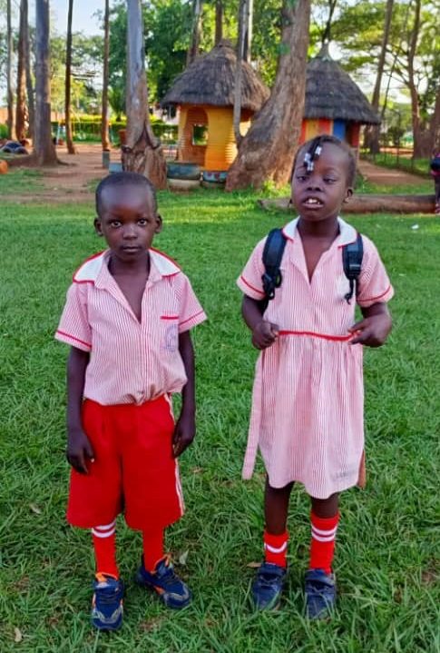 St Monica Feeding 004 Two young Ugandan children in pink and red uniforms stand at St. Monica's Kindergarten