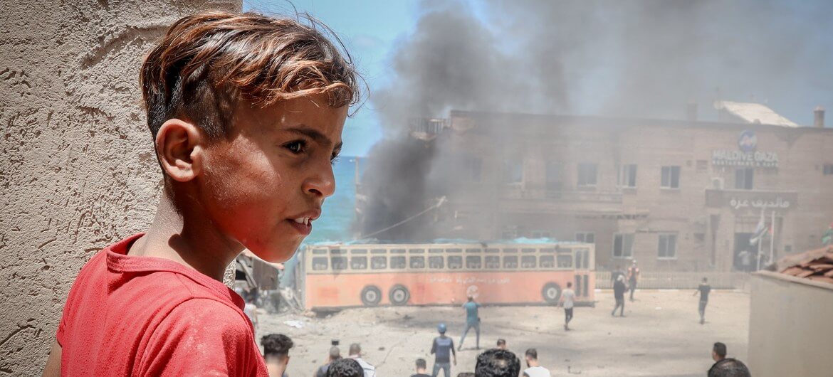 Young boy looks on as fighting takes place around a bus